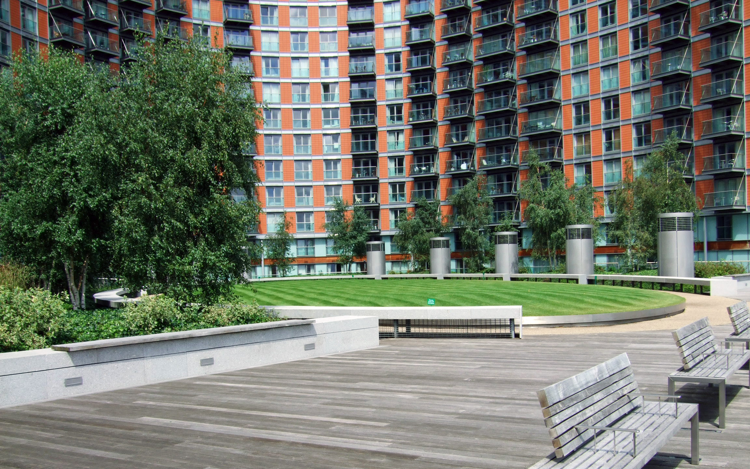 The central courtyard is surrounded by the building and is located on the underground garage. Wooden walkways, benches and lawn in front of a large building